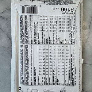 Pode incluir: Um envelope de padrão Simplicity, estilo 8166, com um design de vestido. O envelope branco tem texto e ilustrações em preto, incluindo detalhes de tamanhos e medidas. O preço é de $8,50.