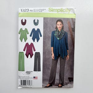 May include: Simplicity sewing pattern 1323 R5 for sizes 14-22. The envelope features illustrations of a tunic with a handkerchief hem, straight-leg trousers, and a cowl neck scarf in green, blue, and maroon. A photograph shows the finished blue tunic.