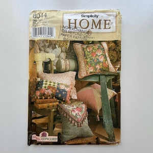 May include: Simplicity Home paper pattern for pillows. The image shows a variety of pillows with floral and patchwork designs. The pattern includes a variety of sizes and styles, with the text "HOME" and "NO EXCHANGE OR REFUND" visible.