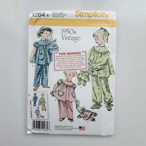 May include: A Simplicity sewing pattern envelope 1264 for children's pyjamas in sizes 3-8. The front features illustrations of children wearing plaid, floral, and solid pyjamas with matching doll outfits. Includes a fire warning label.
