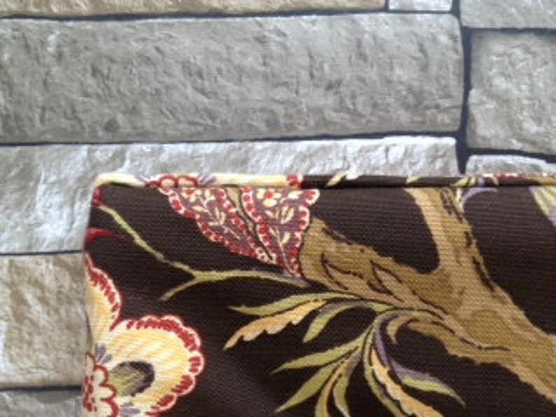 May include: Close-up of a brown fabric with a floral pattern in red, yellow, and cream. The fabric has a dark brown background with a tree branch design. The fabric is likely used for upholstery or home decor.