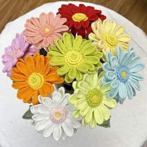 May include: A bouquet of handmade crochet flowers in various colors, including red, pink, orange, yellow, green, white, and blue. Each flower has a detailed center and petals, creating a vibrant and textured display. The flowers are arranged in a circular pattern.