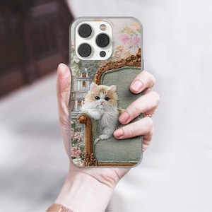 May include: A clear phone case featuring a detailed illustration of a fluffy cat sitting on a green armchair. The background includes a floral design and a small building. The case has a gold-colored frame.