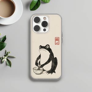 May include: A clear smartphone case featuring a cream-colored background with a black ink-style illustration of a frog holding a small whisk inside a bowl. To the right of the frog, there is a small red square containing the Japanese text 問一.