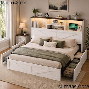May include: A white bed frame with a built-in headboard featuring open shelving and integrated lighting. The bed includes pull-out storage drawers on both sides, containing wire baskets filled with folded textiles. The headboard displays books, a clock, and a digital tablet. The text MirhaasStore appears in the corners.