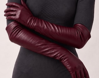 May include: A pair of long, deep burgundy leather gloves that extend past the elbow. The gloves feature a smooth, matte finish and are fitted to the arms, showcasing a classic design with stitched detailing along the fingers and palms.