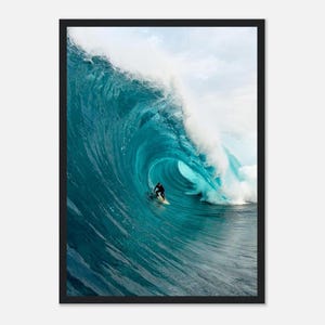 May include: Framed photograph of a surfer riding a large, turquoise wave. The wave is breaking, creating a barrel shape. The surfer is wearing a black wetsuit and riding a white surfboard. The sky is visible in the background.