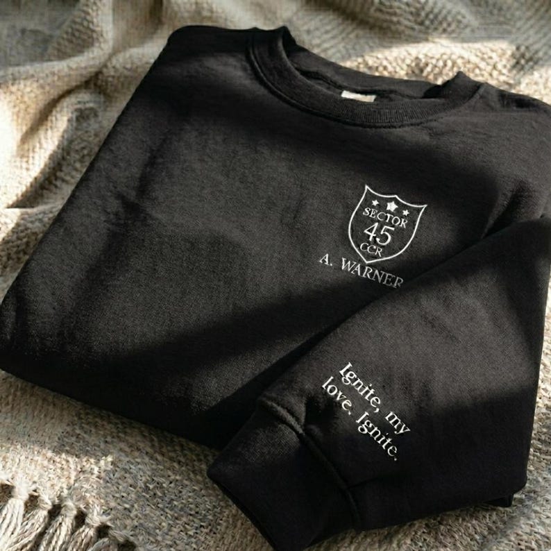 Peut inclure: Sweat-shirt noir &agrave; col rond avec texte brod&eacute; blanc et un &eacute;cusson. L'&eacute;cusson indique "Sector 45 CCR A. Warner". La manche porte l'inscription "Ignite, my love. Ignite."