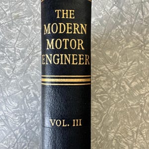 May include: A vintage book spine with the title "THE MODERN MOTOR ENGINEER" in gold lettering. The book is black with gold accents and the volume number "VOL. III" is also in gold.