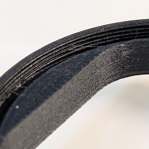 May include: Close-up of a black, textured, circular object. The object appears to be made of multiple layers, with a slightly rough surface. The lighting highlights the texture and shape of the object against a white background.