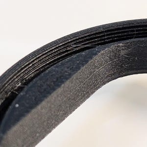 May include: A black circular object with a layered, ridged texture along its outer edge. The surface shows fine horizontal lines and a slightly rough, matte finish, indicating a 3D printed construction with visible filament layers throughout.