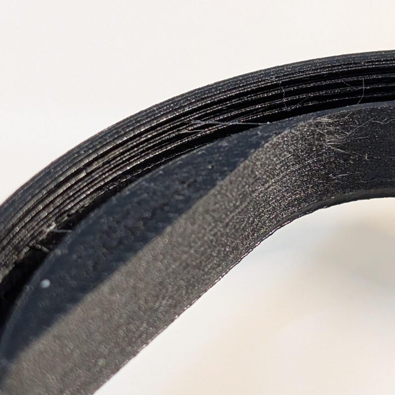 May include: A black circular object with a layered, ridged texture along its outer edge. The surface shows fine horizontal lines and a slightly rough, matte finish, indicating a 3D printed construction with visible filament layers throughout.