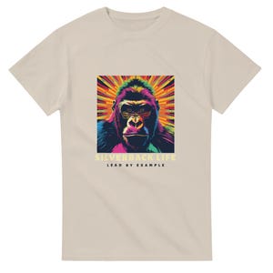 Peut inclure: T-shirt beige avec un graphisme coloré d'un visage de gorille sur un fond rayonnant et vibrant. Le texte "SILVERBACK LIFE" et "LEAD BY EXAMPLE" est imprimé en dessous. Le t-shirt est fait d'une matière douce.