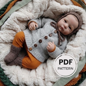 May include: A doll wearing a light gray knitted cardigan with five brown buttons, a matching brown knitted bonnet with ties, mustard yellow ribbed leggings, and brown textured knit socks. A circular white graphic with the text PDF PATTERN is visible.