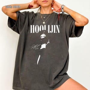 Op de afbeelding: Oversized t-shirt in peperkleur met het woord "HOOLIJIN" in witte letters. Daaronder een witte afbeelding van een persoon met een gezichtsbedekking. Het shirt heeft korte mouwen.