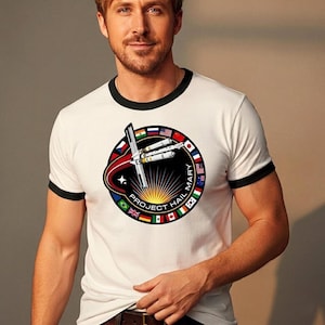 May include: White ringer t-shirt with black trim. The circular graphic features a spaceship design, the text "PROJECT HAIL MARY", and flags of different countries. The design is set against a rising sun.