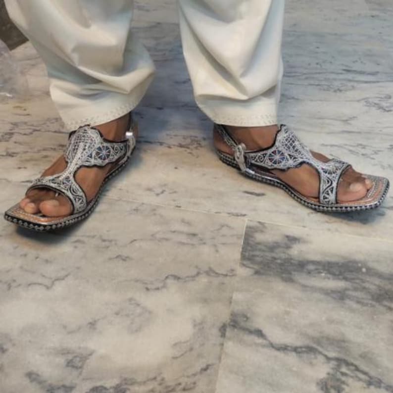 Op de afbeelding: Zilveren en zwarte sandalen met ingewikkelde borduursels. De sandalen hebben een vierkante neus en een enkelbandje. Het ontwerp heeft een gedetailleerd patroon op de bandjes en het voetbed.