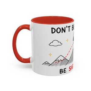 Può includere: Una tazza in ceramica bianca con interno e manico rosso brillante. L'esterno presenta un'illustrazione a cartoni animati di una cima di montagna con un percorso a linee tratteggiate rosse, una nuvola, stelle e il testo "DON'T BE A MOUNTAIN, BE SIGHTSEEING".