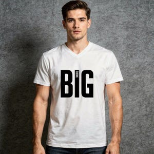 Op de afbeelding: Wit V-hals T-shirt met het woord "BIG" in grote, vette, zwarte letters. Boven het woord "BIG" staat het woord "THINK" in kleinere, zwarte letters. Het shirt is gemaakt van een zacht materiaal.