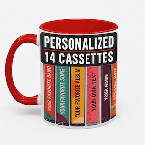 Peut inclure: Un mug en céramique blanche avec un intérieur et une anse rouge vif. L'extérieur présente un graphique de six cassettes avec des étiquettes textuelles incluant PERSONALIZED 14 CASSETTES, YOUR FAVORITE BAND, YOUR FAVORITE SONG, YOUR FAVORITE ALBUM, YOUR OWN TEXT, YOUR NAME et SPECIAL DATE.