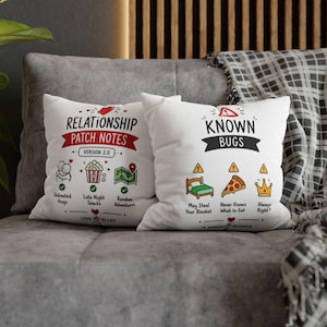 Può includere: Due cuscini quadrati bianchi con grafiche nere, rosse e verdi. Il cuscino a sinistra riporta la scritta Relationship Patch Notes Version 2.0 con icone di abbracci, popcorn e una mappa. Quello a destra riporta Known Bugs con icone di letto, pizza e corona.
