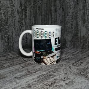 Peut inclure: Un mug en céramique blanche avec une impression graphique représentant un diagramme de réseau neuronal, un ordinateur portable affichant des graphiques, une petite plante, un carnet avec le texte 'data insight model impact' et un mug noir.