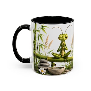 Peut inclure: Un mug en céramique blanche avec une anse et un intérieur noirs, illustré d'un insecte vert méditant en position du lotus sur une tige de bambou, entouré de plantes de bambou, de pierres grises empilées et d'une petite fontaine.
