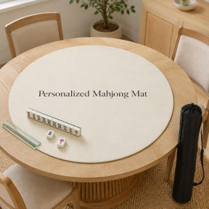 May include: A round, cream-colored mahjong mat with the text Personalized Mahjong Mat printed in black. The mat is placed on a wooden table with a row of mahjong tiles, two loose tiles, a clear tile rack, and a black cylindrical carrying case.