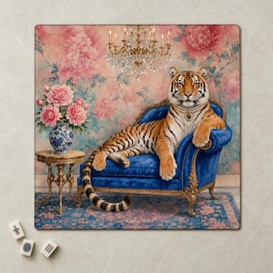 May include: A square wall art print featuring a tiger wearing a pearl necklace, reclining on a blue velvet chaise lounge. Beside it sits a blue and white patterned vase filled with pink peonies on a gold side table under a crystal chandelier.