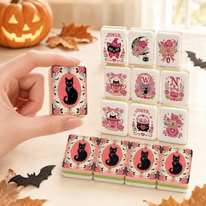 May include: A set of rectangular mahjong tiles featuring black cat illustrations, pink roses, and decorative borders. The tiles display various motifs including a joker, a crescent moon, a teacup, a cauldron, and the letters W and N in pink and green.