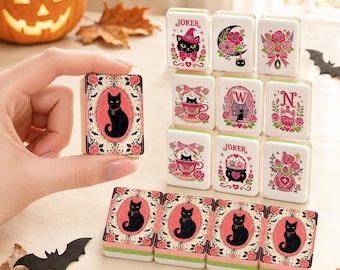 May include: A set of rectangular mahjong tiles featuring black cat illustrations, pink roses, and decorative borders. The tiles display various motifs including a joker, a crescent moon, a teacup, a cauldron, and the letters W and N in pink and green.