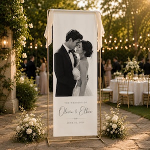 Op de afbeelding: Een hoog, rechthoekig wit welkomstbord voor een bruiloft in een gouden metalen frame. Het bord bevat een zwart-witfoto van een koppel, met de tekst THE WEDDING OF Olivia & Ethan en de datum JUNE 22, 2026 in zwarte letters gedrukt.