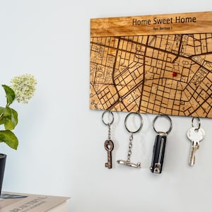 May include: Wooden key holder with a map design and the text "Home Sweet Home." The key holder has several keys hanging from it. A potted plant sits to the left of the key holder.