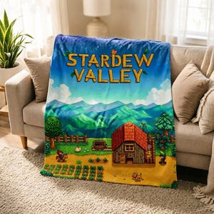 Pu&ograve; includere: Una morbida coperta con il logo del gioco "Stardew Valley" e una vivace scena di fattoria con una casa e montagne. La coperta &egrave; drappeggiata su un divano beige, creando un'atmosfera accogliente.