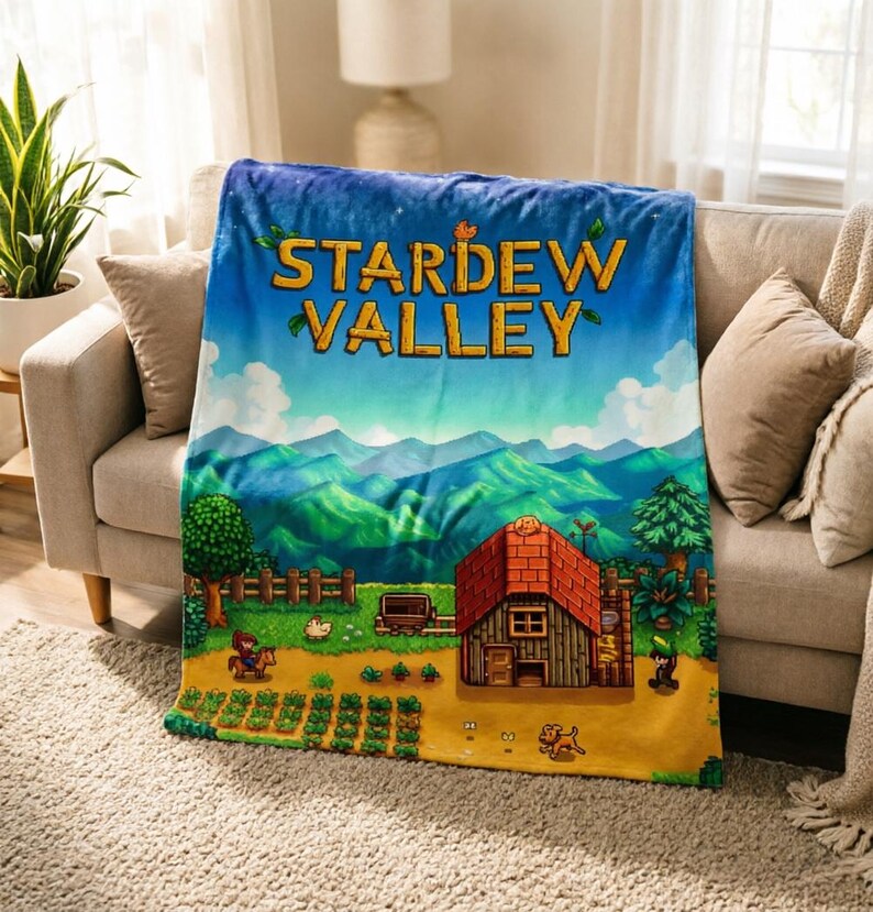 Pu&ograve; includere: Una morbida coperta con il logo del gioco "Stardew Valley" e una vivace scena di fattoria con una casa e montagne. La coperta &egrave; drappeggiata su un divano beige, creando un'atmosfera accogliente.
