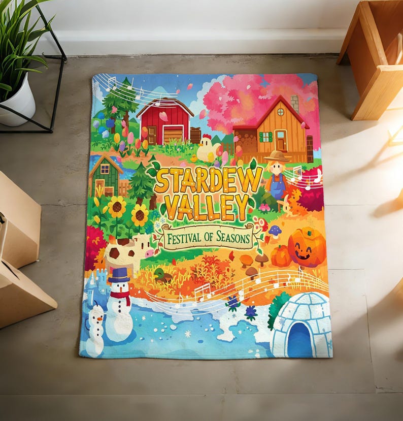 Pu&ograve; includere: Una coperta colorata con la scritta "Stardew Valley Festival of Seasons". Il design include una scena di fattoria con un fienile rosso, una casa, girasoli, pupazzi di neve e una zucca. La coperta ha uno stile vivace e fumettistico.