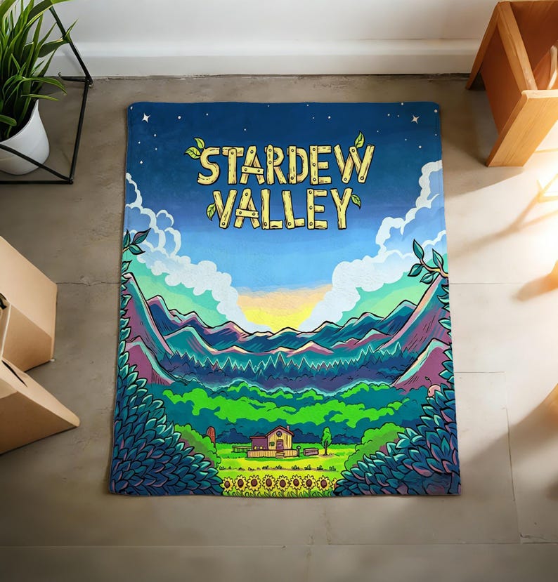 Pu&ograve; includere: Una coperta rettangolare con un'illustrazione colorata di un paesaggio e la scritta "STARDEW VALLEY". Il design include montagne, una casa, girasoli e un cielo blu con nuvole. La coperta &egrave; probabilmente in tessuto morbido.