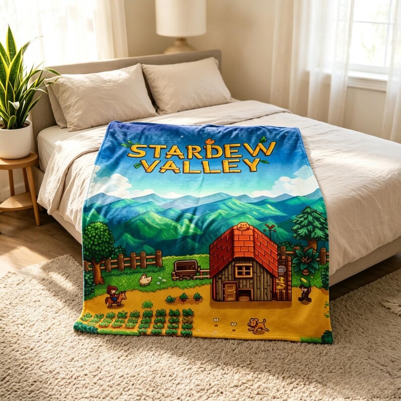 Pu&ograve; includere: Una coperta blu con la scritta "STARDEW VALLEY" e un paesaggio colorato. Il design include una casa con il tetto rosso, colline verdi e un campo con colture. &Egrave; raffigurata anche una persona a cavallo e un cane.