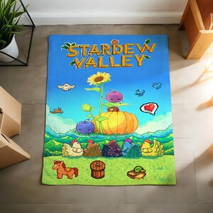 Pu&ograve; includere: Un tappeto rettangolare blu e verde a tema Stardew Valley. Il tappeto presenta grafiche pixelate di un girasole, una zucca e vari animali da fattoria. Le parole "STARDEW VALLEY" sono in alto in giallo e verde.