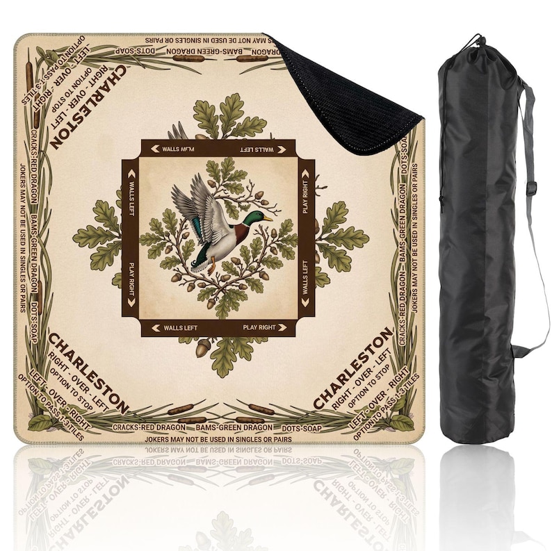 May include: A square game mat with a duck illustration, oak leaves, and text reading "Charleston." The mat is beige with brown and green accents. A black carrying bag is included. The game mat is designed for a board game.