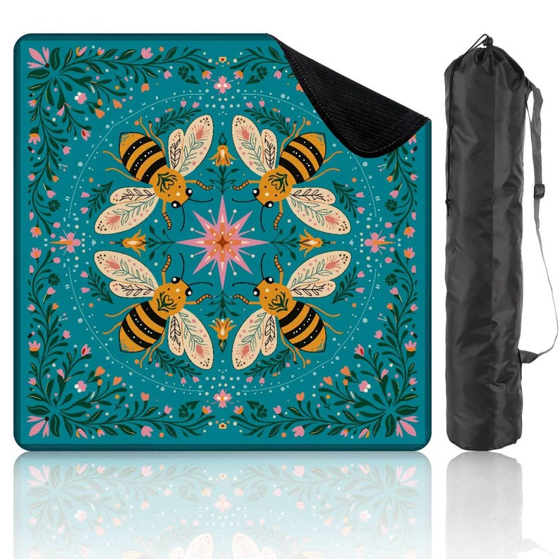 May include: A teal picnic blanket with a bee and floral design. The blanket features four large bees with yellow and black stripes, surrounded by pink and white flowers. A black carrying bag is included.
