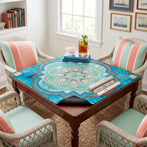 May include: A square, wooden game table with a turquoise, patterned mat featuring oyster and seashell designs. The table is surrounded by four wicker chairs with striped pillows. A pitcher of iced tea and books are on the table. The room has a coastal theme.