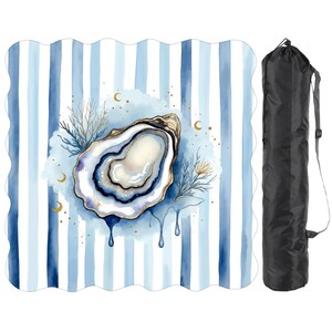 May include: A beach blanket featuring a watercolour oyster design on a blue and white striped background. The oyster has gold accents and a blue interior. A black carrying bag is included.