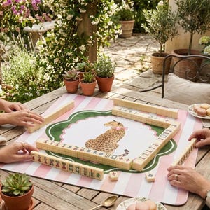 Op de afbeelding: Een witte keramische mok met een zwart handvat en de tekst "But First, Coffee" in een vetgedrukte, zwarte letter. De mok is gevuld met een donkere vloeistof, waarschijnlijk koffie, en staat op een lichtgekleurd oppervlak.