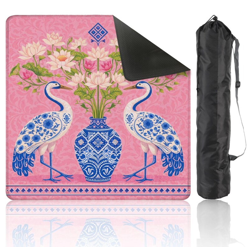 May include: Pink yoga mat with a floral and bird design. The mat features two white and blue cranes facing each other, a blue vase with flowers, and a black carrying bag. The mat has a decorative border and a patterned background.