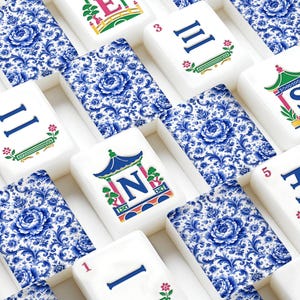 May include: A set of rectangular mahjong tiles featuring a blue and white floral pattern on the back. The front of the tiles displays colorful illustrations of pagodas with letters, Roman numerals, and small floral accents in red and green.