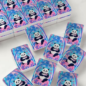 May include: A collection of rectangular tiles featuring a colorful illustration of a panda sitting on a pink rock, surrounded by blue bamboo stalks and pink flowers. The design includes small hanging lanterns and a vibrant blue and pink color palette.