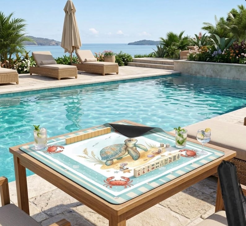 May include: A wooden table with a blue and white patterned mat featuring a sea turtle and crab design. The table holds mahjong tiles, dice, and drinks, set against a pool and ocean backdrop.