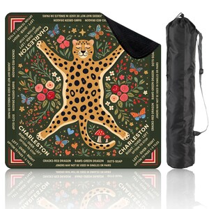 May include: A square, green Charleston game mat featuring a cheetah design with floral and butterfly accents. The mat includes game instructions and comes with a black carrying bag for easy transport.
