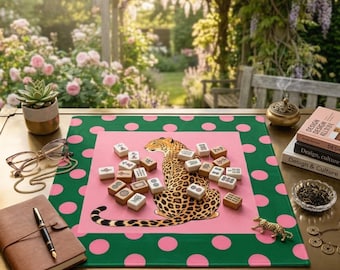 May include: A pink and green polka dot mat with a leopard illustration and mahjong tiles. A succulent in a gold pot, eyeglasses, a leather journal, and books are also on the table. A small gold leopard figurine is in the foreground.